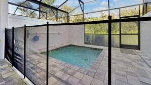 A swimming pool with a glass enclosure, surrounded by a metal fence, and a view of trees and sky through the structure. - Relaxing Nature Escapade with Game Room (Clermont)