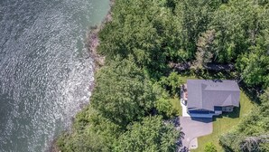 Eine Vogelperspektive eines Hauses, das von dichtem Wald und einem Gewässer umgeben ist.