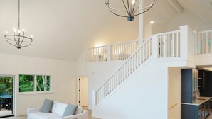 A spacious living area with a white staircase, a dining area, and a kitchen with dark cabinets. - Luxury Waterfront Home in Suttons Bay (Suttons Bay)