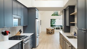 A modern kitchen with grey cabinets, stainless steel appliances, and a wooden dining table. - Luxury Waterfront Home in Suttons Bay (Suttons Bay)
