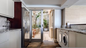 Une cuisine moderne équipée d’un lave-linge intégré et d’une porte vitrée donnant sur un patio agrémenté de plantes.