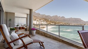 Un balcon avec vue sur la mer et les montagnes, aménagé avec des chaises et un petit coin salon.