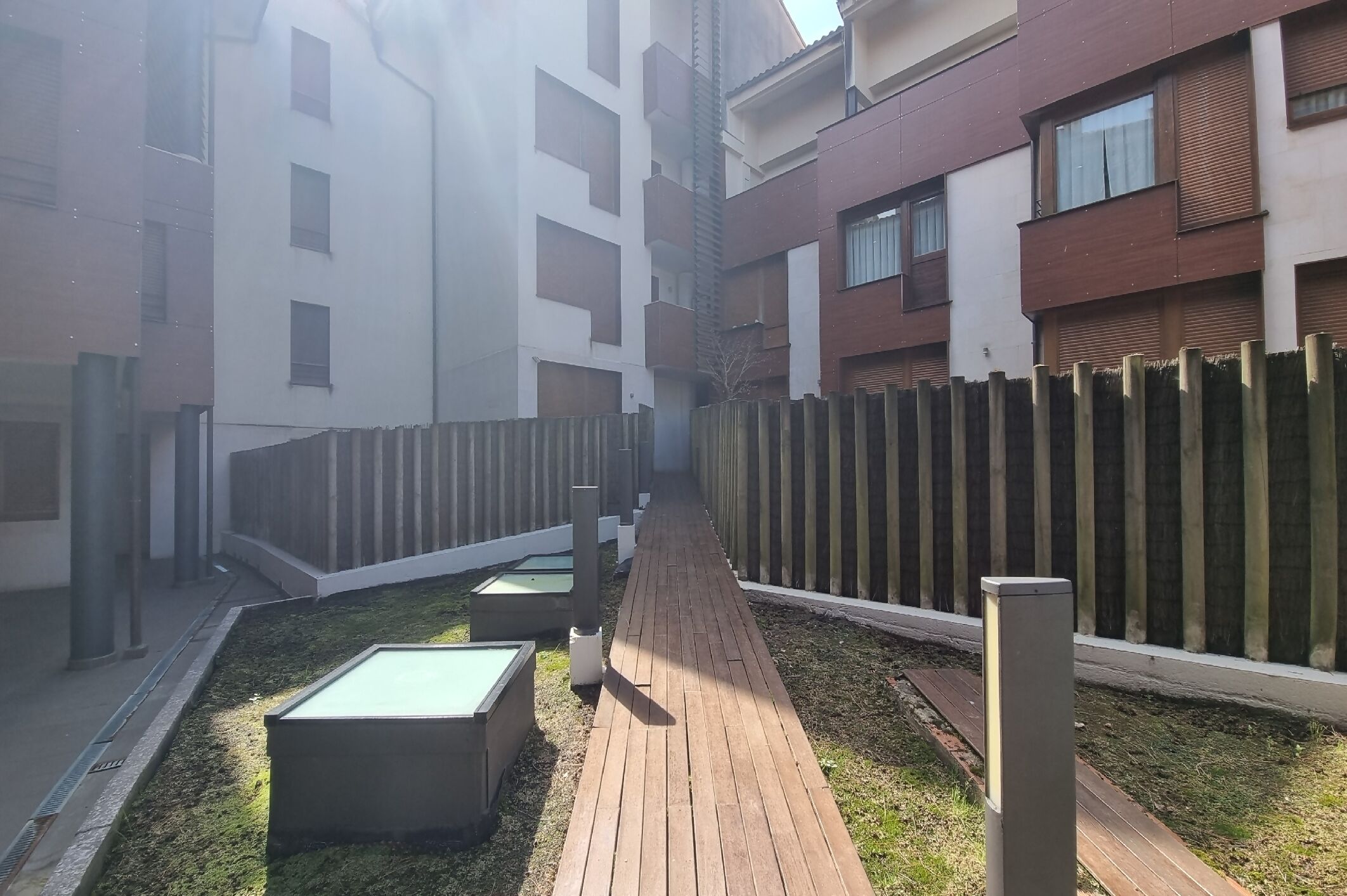 Une cour avec un chemin en bois, des bancs et une clôture.