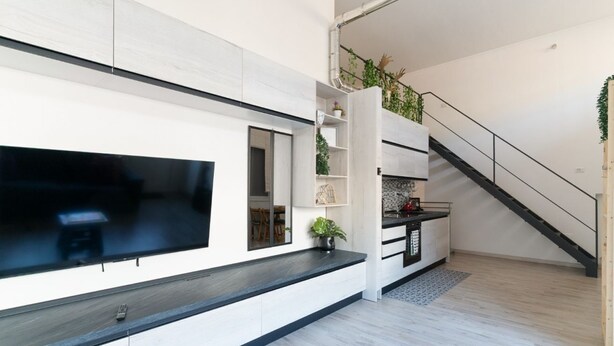Un salon moderne doté d’un téléviseur à écran plat, d’étagères intégrées, d’un escalier et d’une plante en pot.