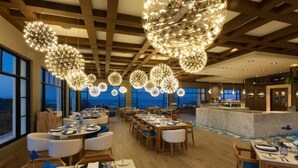 A restaurant with multiple dining tables and chairs, large hanging spherical light fixtures, and a view of the outside through large windows. - 3-bedroom resort in wonderful Cabo San Lucas with WiFi, fitness room (Cabo San Lucas)