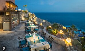 Zona de dinar a l'aire lliure amb taules i cadires, amb vistes al mar.