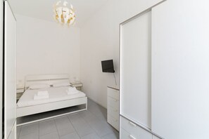 A bedroom with a bed, a TV, a wardrobe, and a chandelier.