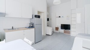 Eine moderne Küche mit weißen Schränken, einer Mikrowelle und einem Kühlschrank. Ein Esstisch mit Stühlen steht ebenfalls dort.