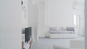 Ein schlicht eingerichtetes Wohnzimmer mit Flachbildfernseher, Sofa und weißer Wand.
