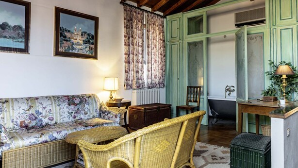 A room with a sofa, wicker chairs, a table, a cabinet, and a radiator.