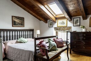 A bedroom with a wooden ceiling, a bed with a headboard, a bench, a dresser, and framed pictures on the walls.
