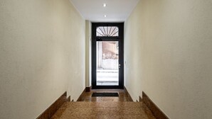A hallway with a black door, white walls, and a tiled floor.