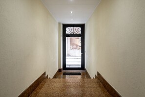 Un pasillo con una puerta negra, paredes blancas y piso de baldosas.
