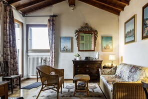 Una habitación con techo de madera, un sofá de mimbre, un aparador de madera, un espejo y cuadros enmarcados en la pared.