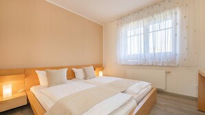A double bed with a wooden headboard, two bedside tables with lamps, a window with sheer curtains, and a radiator.