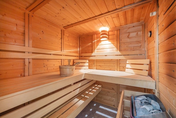 A sauna with wooden benches, a bucket, and a stone-filled container.