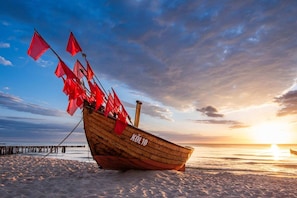 A wooden boat with red flags on a sandy beach at sunset.