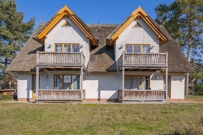 A two-story house with a thatched roof, wooden balconies, and a white exterior.