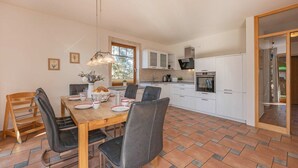 A modern kitchen with white cabinets, a dining table with chairs, and a large window.