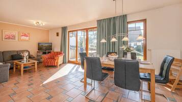 A living room with a sofa, coffee table, TV, and a dining area with chairs and a table.
