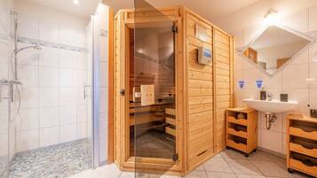 Una sauna de madera con puerta de vidrio, zona de ducha y lavamanos con armarios de madera.