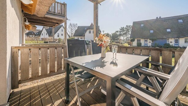 A covered outdoor seating area with a table and chairs, a grill, and a view of houses in the background.