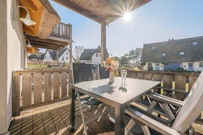 A covered outdoor seating area with a table and chairs, a grill, and a view of houses in the background.