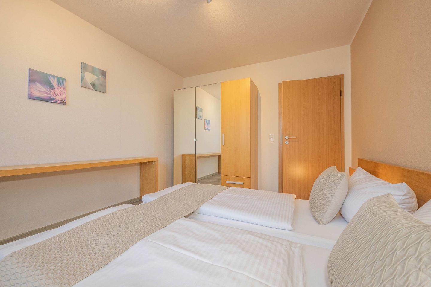 Une chambre d’hôtel avec deux lits, une tête de lit en bois, une table de chevet, un miroir et deux tableaux accrochés au mur.