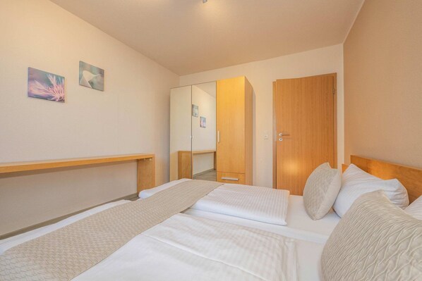 A hotel room with two beds, a wooden headboard, a bedside table, a mirror, and two wall-mounted paintings.