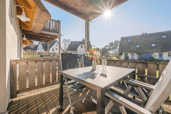 A covered outdoor seating area with a table and chairs, a grill, and a view of houses in the background.