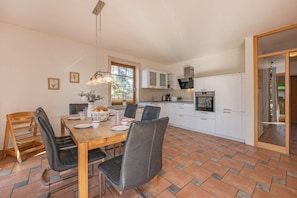 A modern kitchen with white cabinets, a dining table with chairs, and a large window.