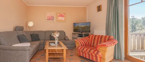 Un salon comprenant un canapé, un fauteuil en osier, une table basse, un téléviseur et des œuvres d’art accrochées au mur.