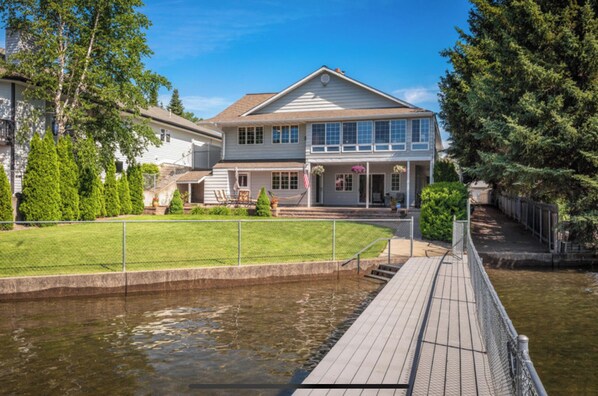 A two-story house with a dock extending into a body of water, surrounded by greenery and trees. - River's Edge Oasis, private dock, 2 kitchens, pool table, dog friendly! (Post Falls)
