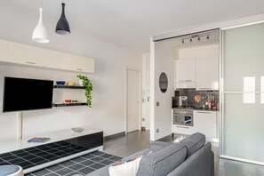 A modern living room with a flat-screen TV, a sofa, a coffee table, and a kitchen area with cabinets and appliances.