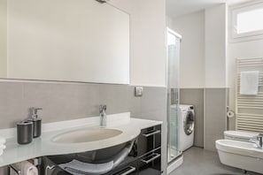 A modern bathroom with a glass shower enclosure, a built-in washing machine, and a separate toilet.