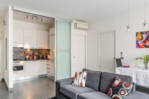 A modern kitchen with white cabinets, a dining area with a table, and a gray sofa with patterned cushions.