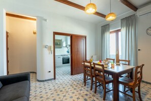 A dining area with a table and chairs, a sofa, and a kitchen in the background.