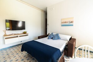 Un dormitorio con cama, televisión, un cuadro y una silla blanca.