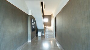 Un couloir avec un escalier, une poubelle et une porte sur laquelle sont accrochés des papiers.