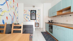 A modern kitchen with light blue cabinets, a wooden dining table, and a gray sofa. - GuestHost - Gelsomini Apartment Milano (Milano)