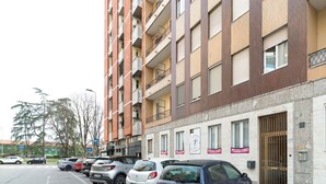 A multi-story residential building with balconies, a parking lot, and several commercial establishments on the ground floor. - GuestHost - Gelsomini Apartment Milano (Milano)