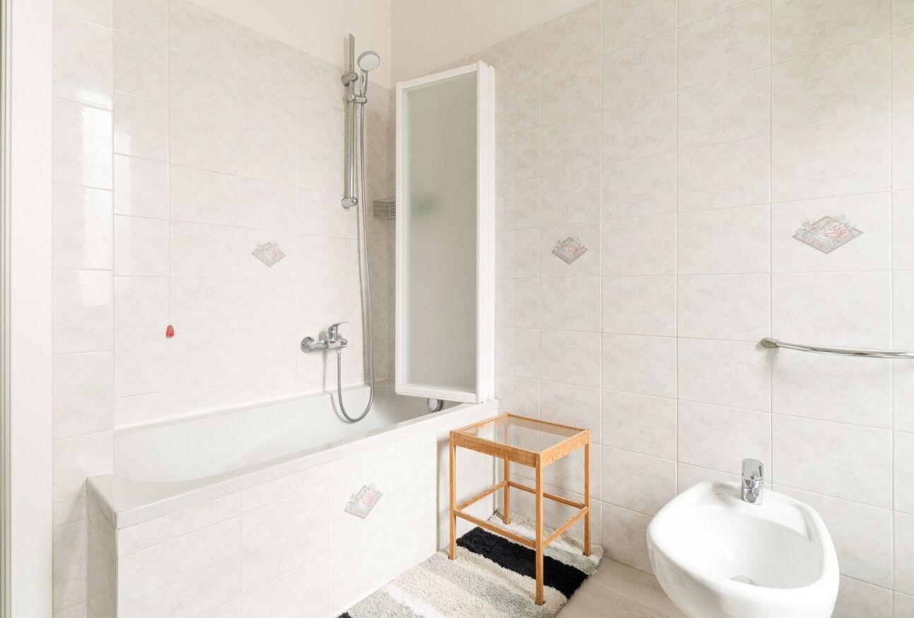Een badkamer met een bad, een douche, een klein houten krukje en een bidet.