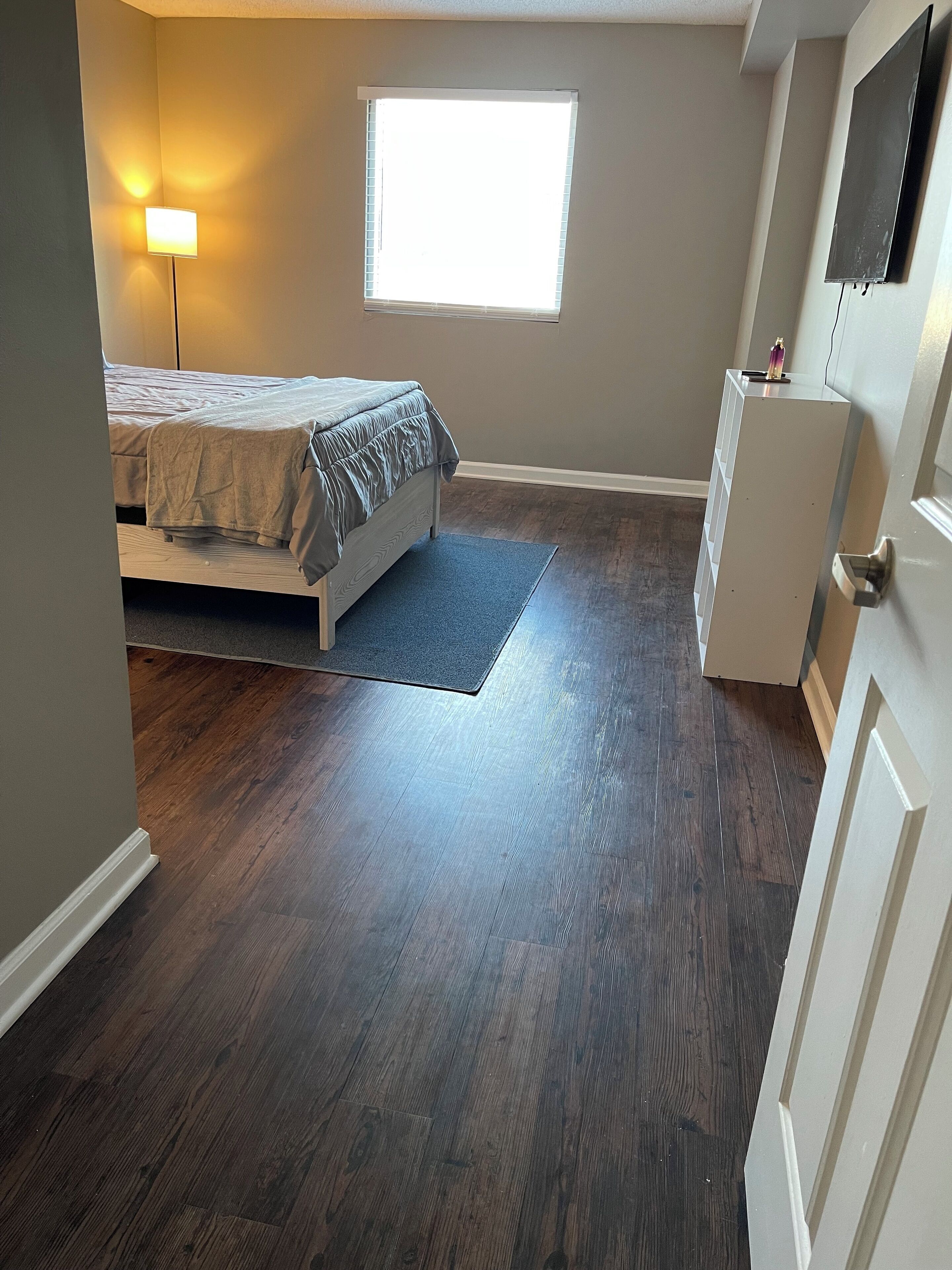 A bedroom with a bed, a nightstand, a dresser, a window, and a door.