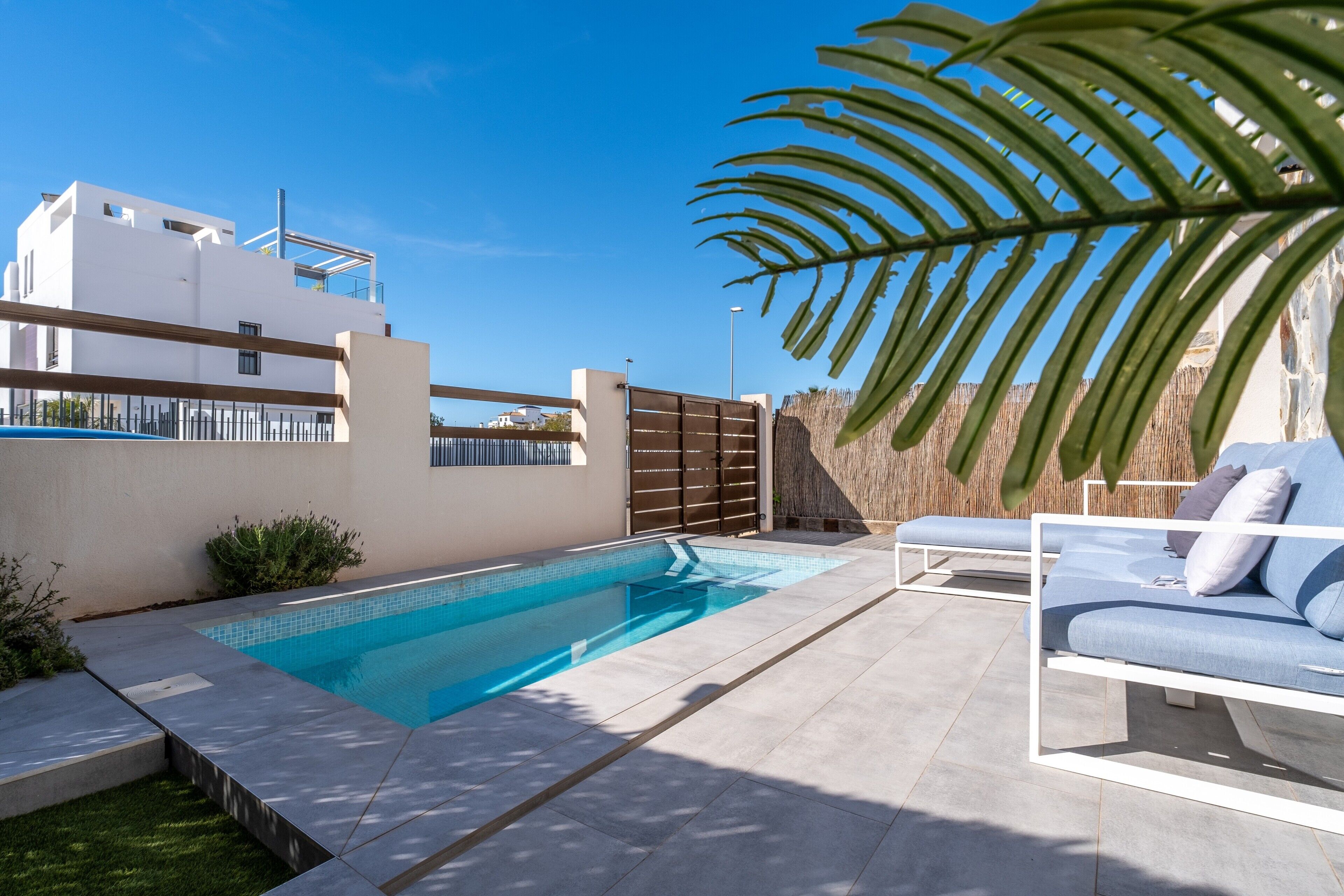 Un espace piscine extérieur moderne, avec des chaises longues, une piscine et un bâtiment blanc en arrière-plan.