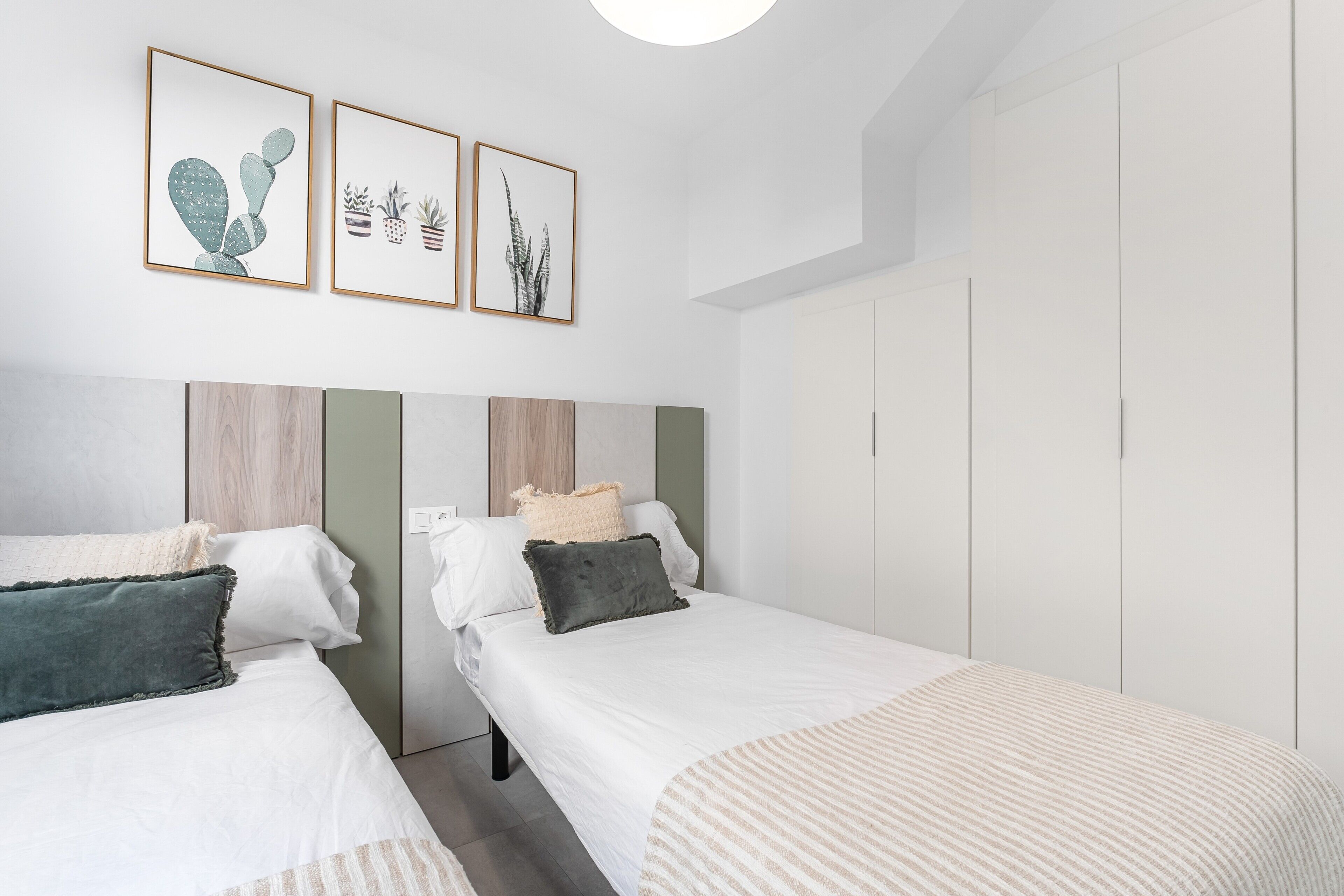 A bedroom with two beds, a wardrobe, and three framed pictures on the wall.