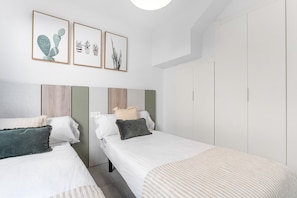A bedroom with two beds, a wardrobe, and three framed pictures on the wall.