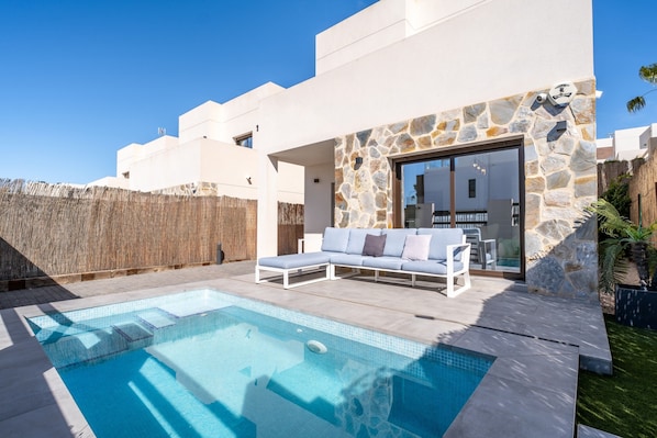 A modern house with a swimming pool, a white outdoor seating area, and a stone wall.
