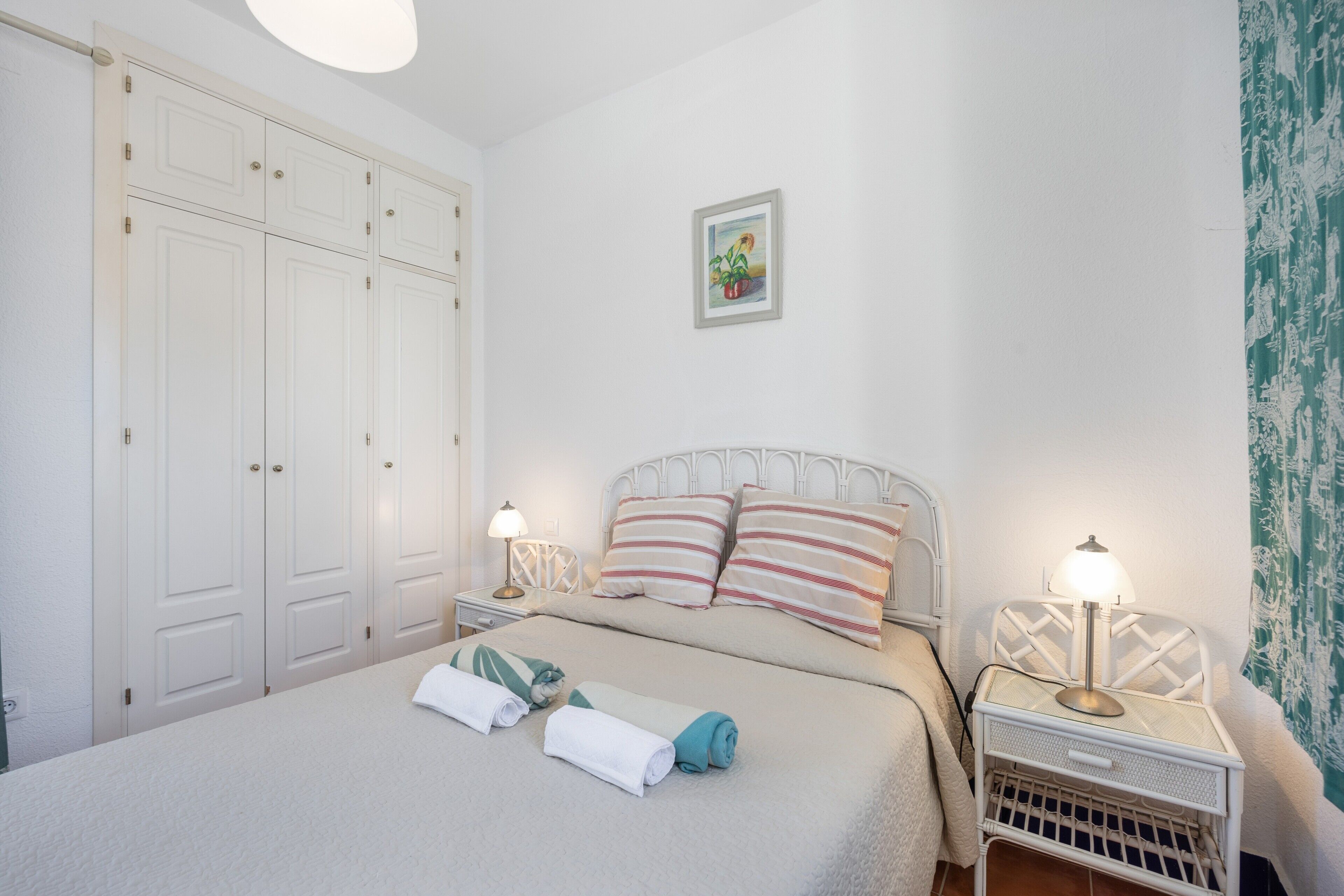 A bedroom with a bed, two bedside tables with lamps, a wardrobe, and a wall-mounted picture.
