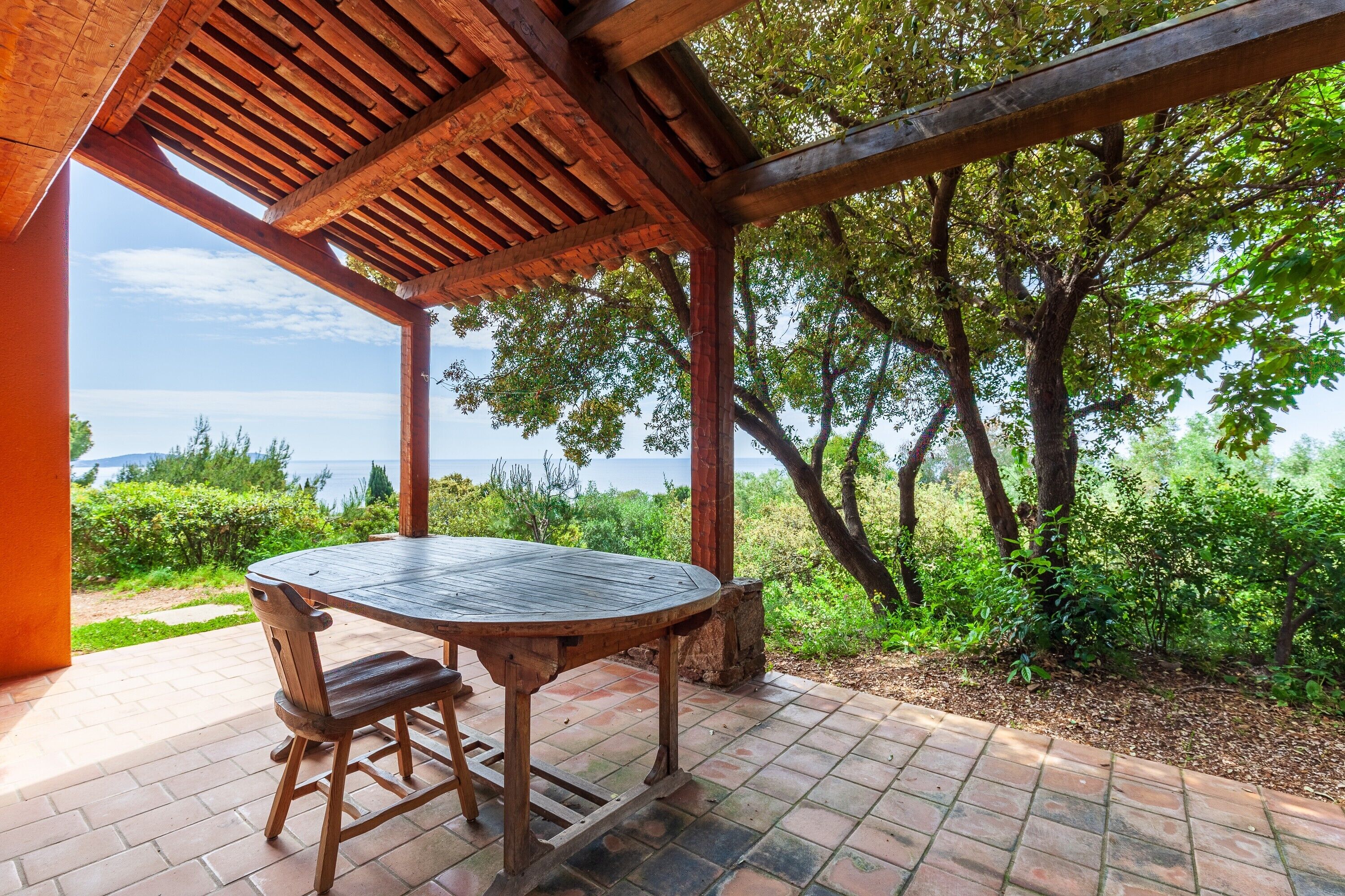 Une pergola en bois, avec une table et des chaises, offrant une vue panoramique sur un paysage arboré et un plan d’eau.