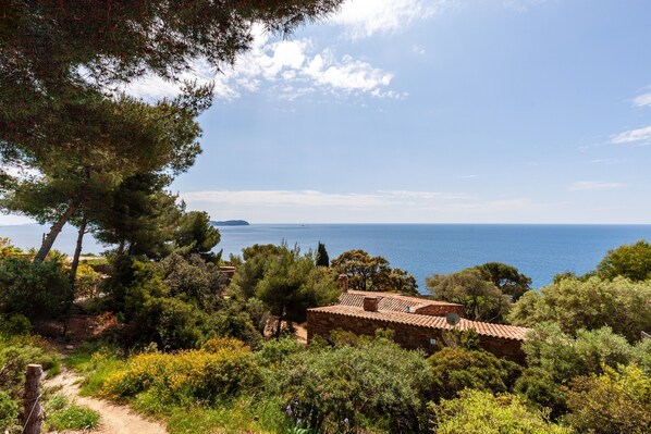 A coastal landscape with a stone building, trees, and a clear view of the sea.